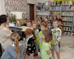 Uczniowe słuchają pani bibliotekarki w bibliotece