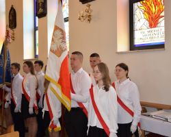 Grupa uczniów stoi ze sztandarami w kościele