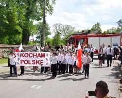 Grupa uczniów ubranych na galowo stoi z flagami i transparentem Kocham polskę
