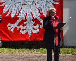 Kobieta przemawia przez mikrofon przy godle Polski