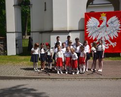 Grupa małych dzieci ubranych na galowo śpiewa piosenki patriotyczne