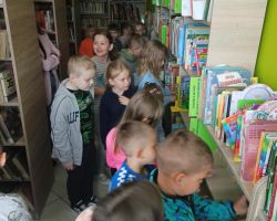 Uczniowie ogładają regały z książkami w bibliotece.