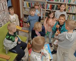 Uczniowie stoją w bibliotece i trzymają w rękach książki.