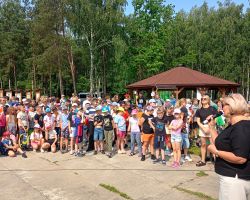 Kobieta przemawia do zgromadzonych uczniów w plenerze.