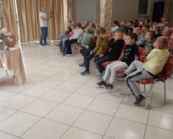 Uczniowie siedzą na krzesłach i słuchają mężczyzny, który stoi przed nimi.