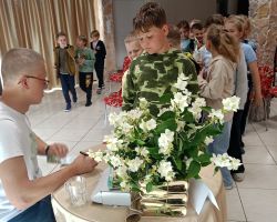Mężczyzna siedzi przy stoliku i podpisuje dzieciom książki.