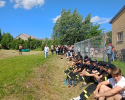 Ludzie siedzą na trawie i oglądają zawody sportowo-pożarnicze.
