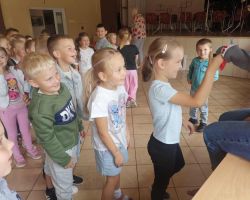 Dzieci stoja w kolejce do mskotki, którą trzyma pani bibliotekarka