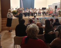 Na zdjęciu panowie składają życzenia i wręczają kwiaty pani dyrektor goku