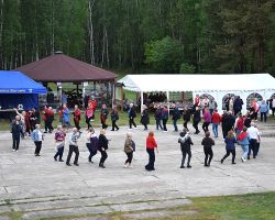 Na zdjęciu ludzie bawią się i tańczą w kole pod gołym niebiem