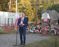 zdjęcie przedstawia osobę przemawiającą pod pomnikiem