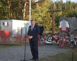 zdjęcie przedstawia osobę przemawiającą pod pomnikiem