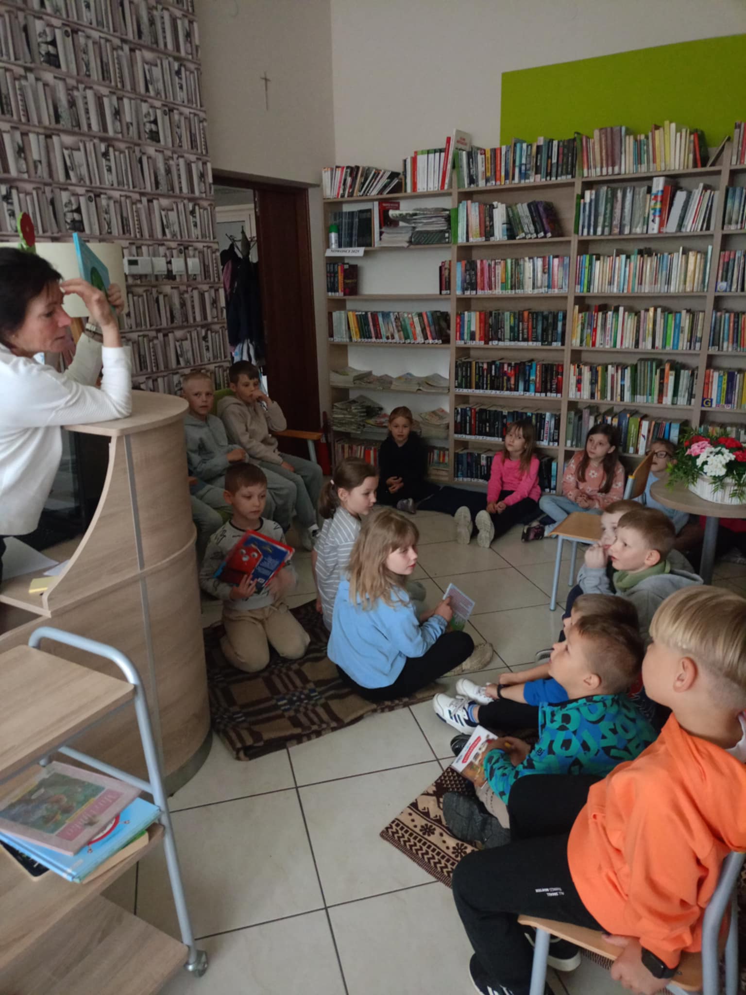 Uczniowie słuchają pani bibliotekarki w bibliotece.