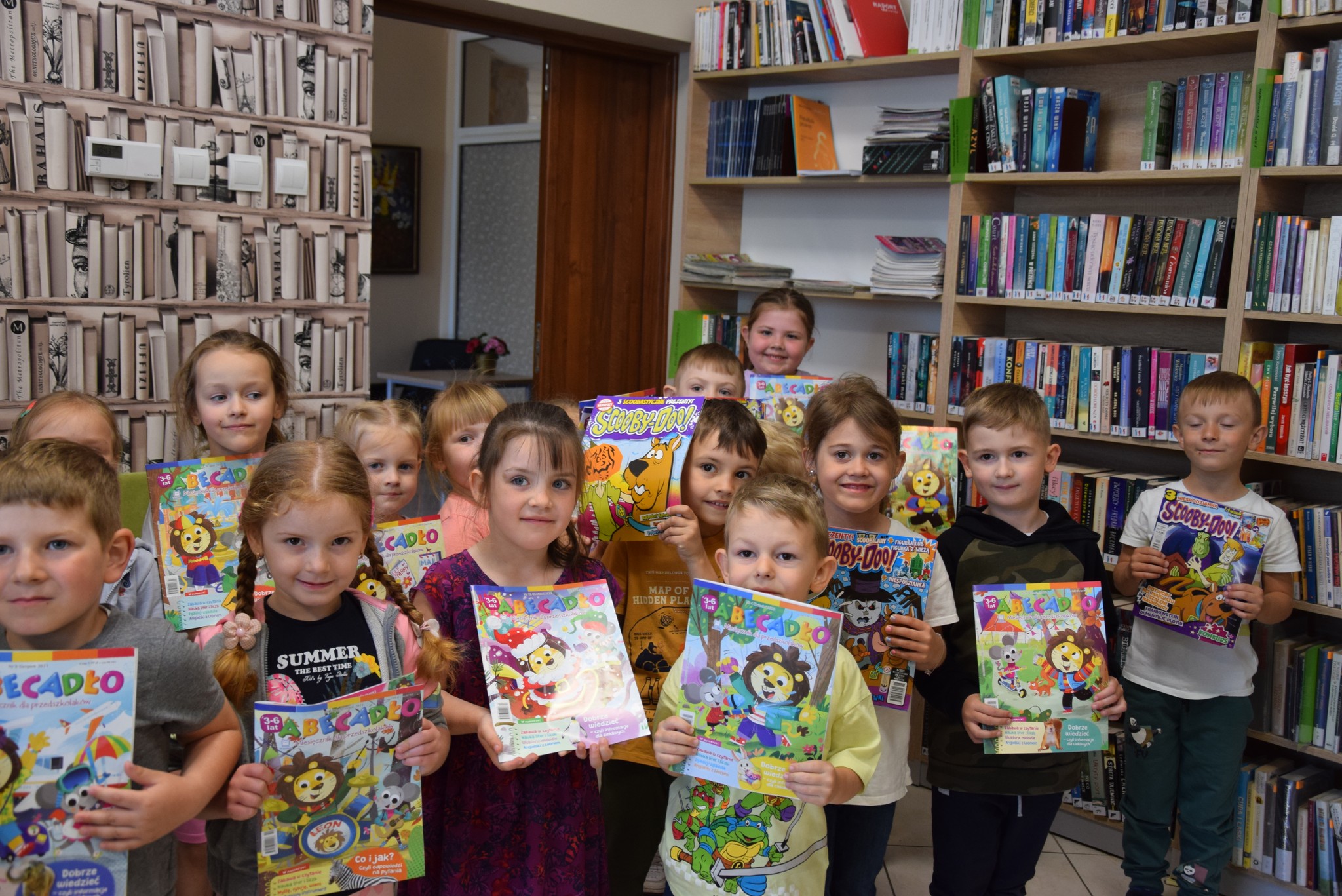 Zdjęcie grupowe dzieci z gazetkami w bibliotece.